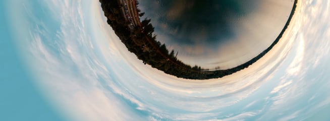 Panoramic view of a serene lake surrounded by trees and clouds, creating a spherical effect.