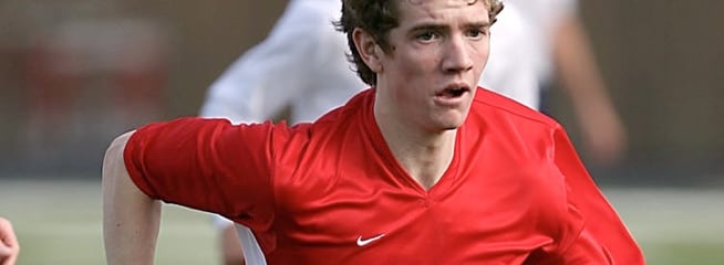 Young soccer player in a red jersey running intensely during a match.